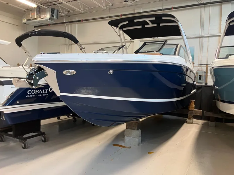 Slide: The Image of 2025 Cobalt R6 boat in showroom, blue hull, white trim, elevated on blocks. - 2