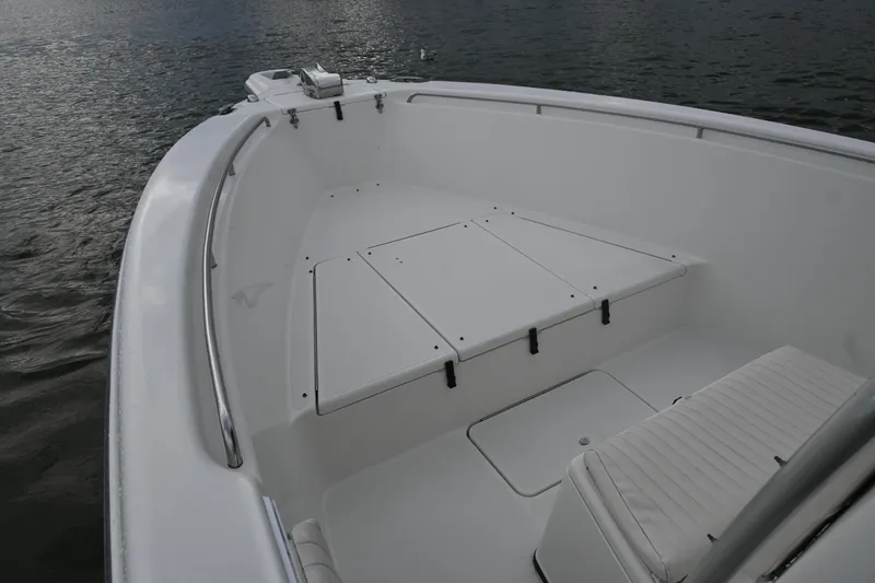 Slide: The Image of 2002 Triton 2895 CC boat interior with white seating and storage compartments on calm water. - 11