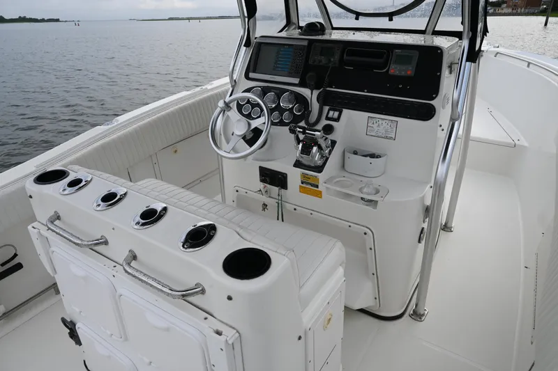 Slide: The Image of 2002 Triton 2895 CC boat cockpit with steering wheel and control panel on calm water. - 24