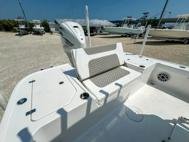 Slide: The Image of 2024 Caymas 28 HB boat with cushioned seating and outboard motor in a sunny marina. - 12