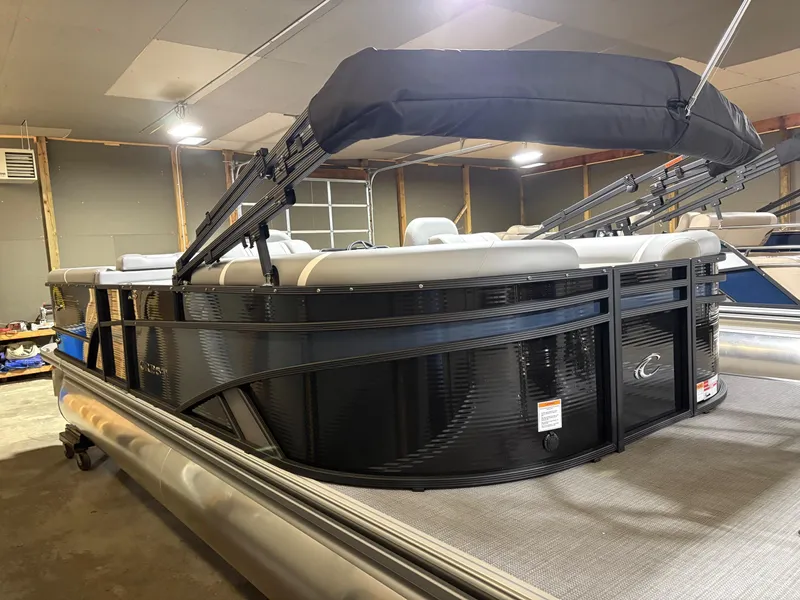 Slide: The Image of 2025 Crest 240 SLC pontoon boat in a garage, featuring sleek black design and canopy. - 2