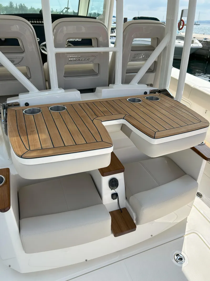 Slide: The Image of 2025 Boston Whaler 360 Outrage boat interior with teak table and cushioned seating. - 19