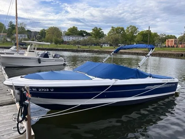 The Image of 2006 Bayliner 215 Classic boat docked on a calm river with blue cover. - 0