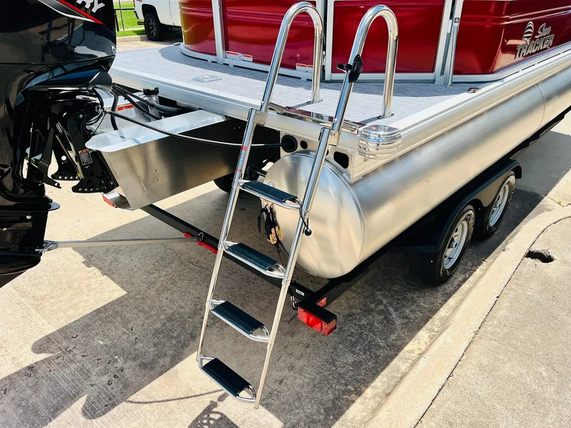 Slide: The Image of 2026 Sun Tracker Party Barge 20 DLX with ladder and trailer, parked on concrete. - 9