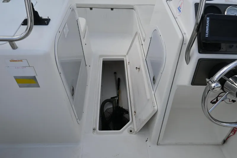 Slide: The Image of 1999 Aquasport 215 Dual Console boat storage compartment with open hatch and visible equipment. - 13
