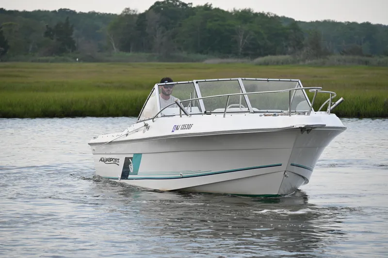 Slide: The Image of 1999 Aquasport 215 Dual Console boat cruising on a calm river with lush greenery. - 3