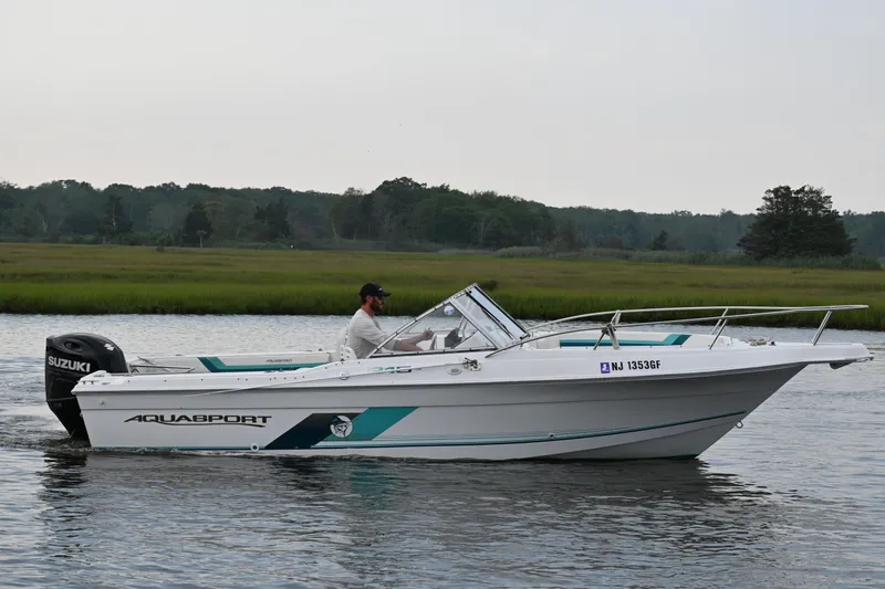Slide: The Image of 1999 Aquasport 215 Dual Console boat cruising on a calm river with lush green background. - 4