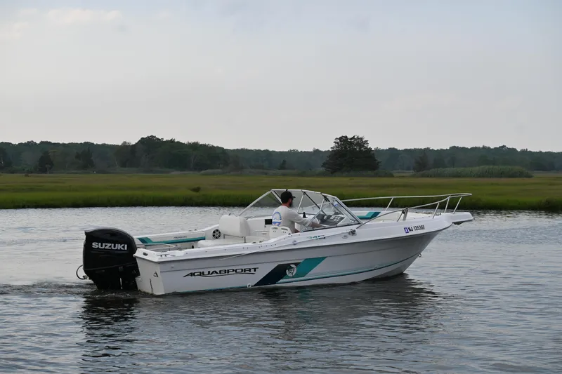 Slide: The Image of 1999 Aquasport 215 Dual Console boat cruising on a calm river with Suzuki outboard motor. - 5