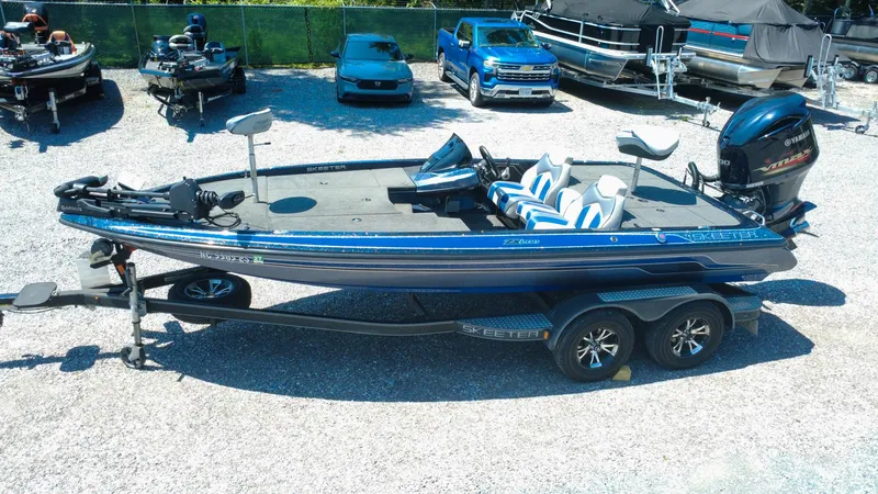 Slide: The Image of 2021 Skeeter ZX200 boat on trailer, parked in a gravel lot with other vehicles. - 2