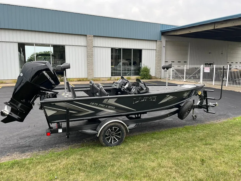 Slide: The Image of 2026 Lund 1875 Pro-V Bass XS boat on trailer, parked outside a building. - 1