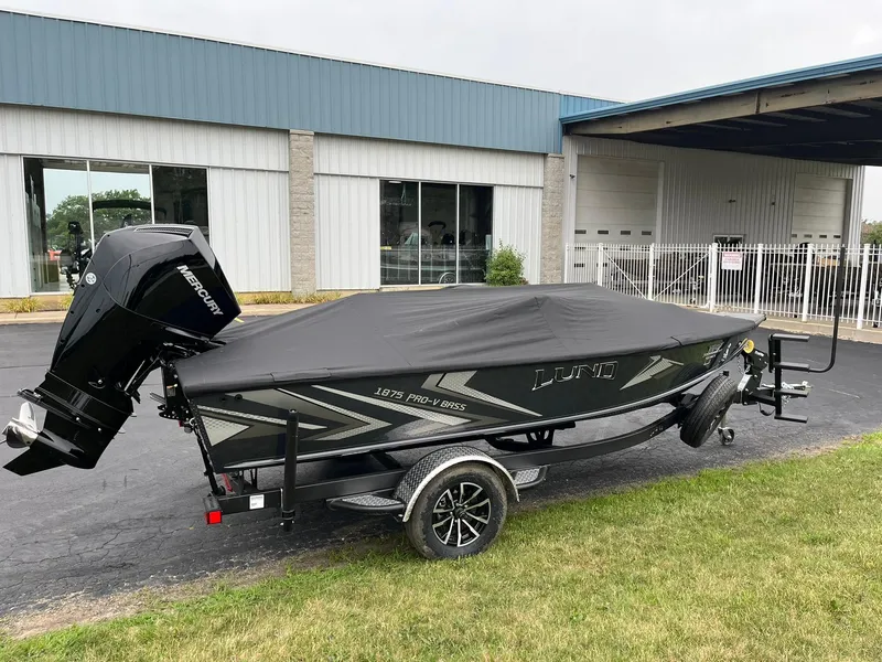 Slide: The Image of 2026 Lund 1875 Pro-V Bass XS boat with cover and Mercury engine, parked outside. - 24