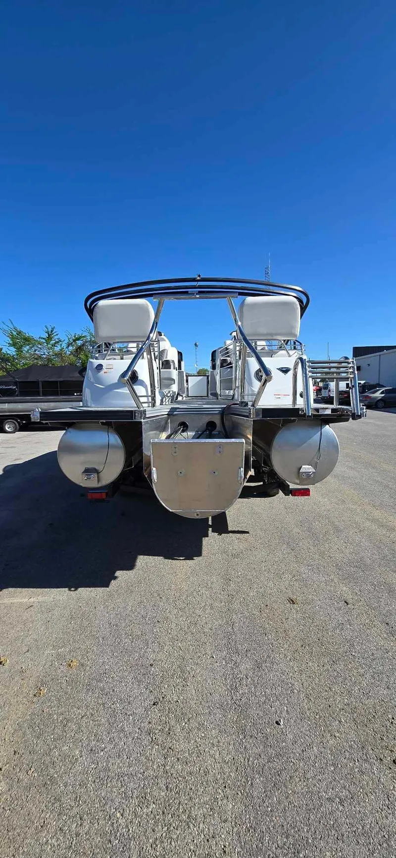 Slide: The Image of 2025 Manitou 25 LX SRW pontoon boat, rear view, parked on pavement under clear blue sky. - 10