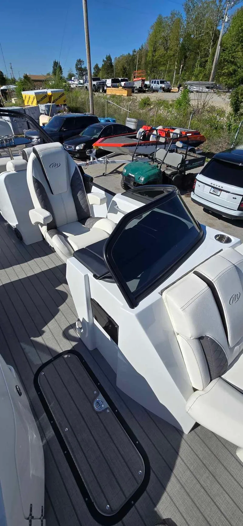 Slide: The Image of 2025 Manitou 25 LX SRW boat with sleek seating and modern dashboard, parked outdoors. - 13