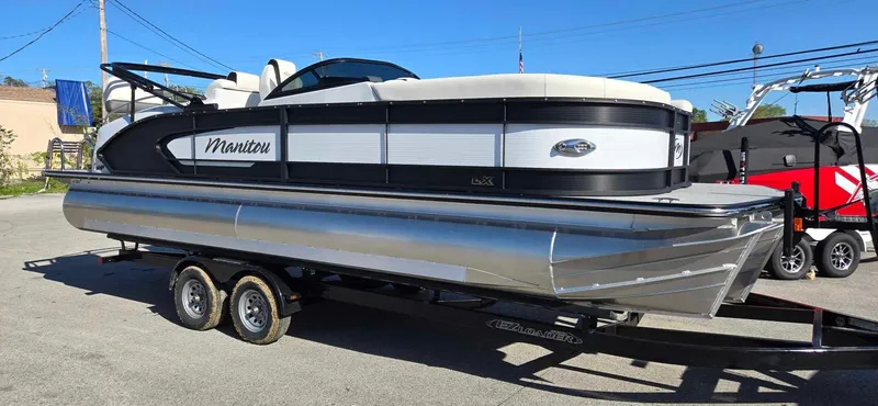 Slide: The Image of 2025 Manitou 25 LX SRW pontoon boat on trailer, sleek design, parked outdoors. - 4