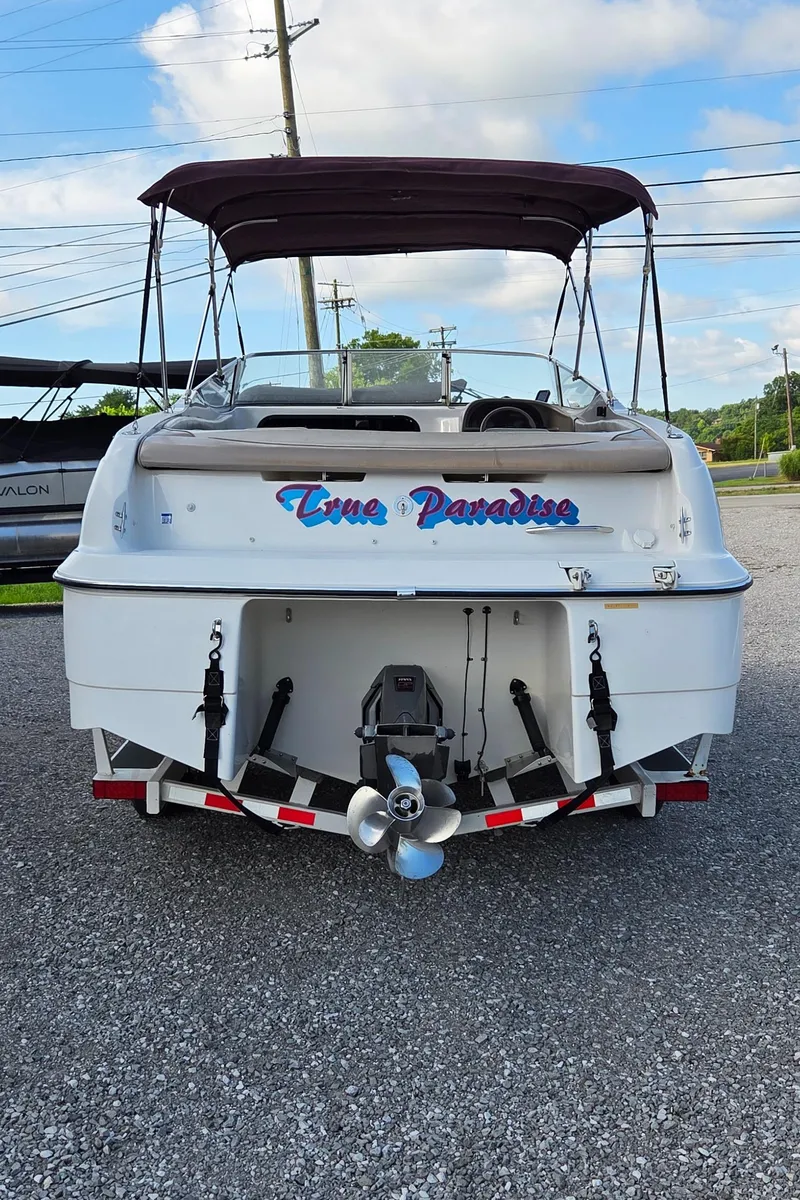 Slide: The Image of 1995 Four Winns 245 Sundowner boat, rear view, named "True Paradise," parked on gravel. - 2