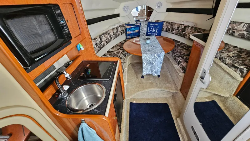 Slide: The Image of 2003 Rinker Fiesta Vee 270 cabin interior with kitchenette, dining area, and cozy seating. - 13