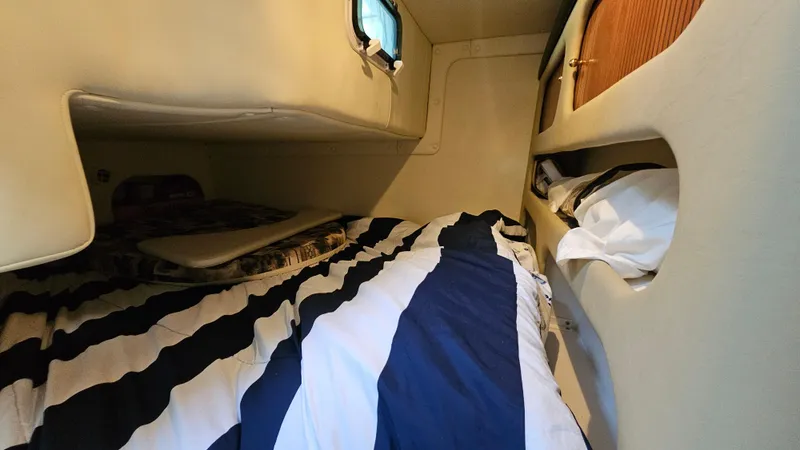 Slide: The Image of 2003 Rinker Fiesta Vee 270 cabin interior with striped bedding and storage compartments. - 18