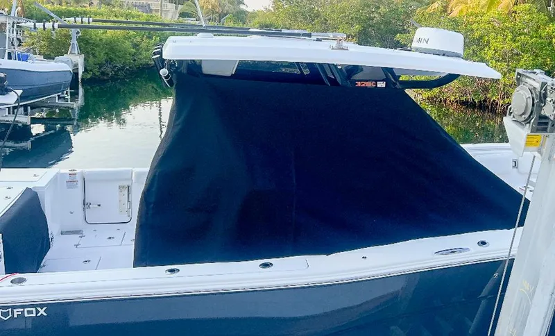 Slide: The Image of 2024 Sea Fox 328 Commander boat with black cover, docked near lush greenery. - 22