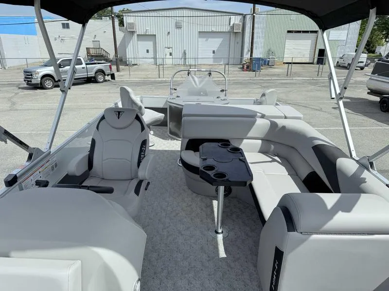 Slide: The Image of 2025 Trifecta 22TRFC LE pontoon boat interior with seating and table, parked in industrial area. - 3