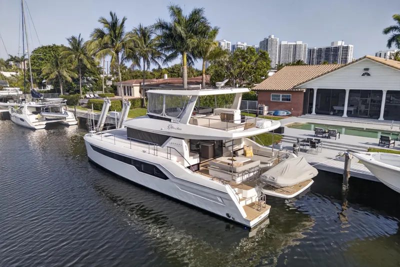 Slide: The Image of 2022 Leopard 53 Powercat yacht docked by waterfront home with palm trees. - 2