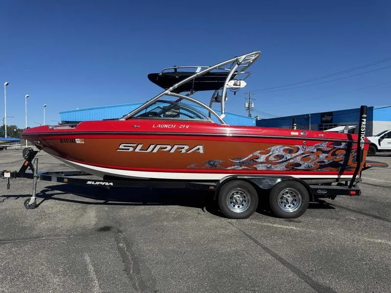 Slide: The Image of 2009 Supra 21V LAUNCH boat on trailer, vibrant red with flame graphics, parked outdoors. - 0