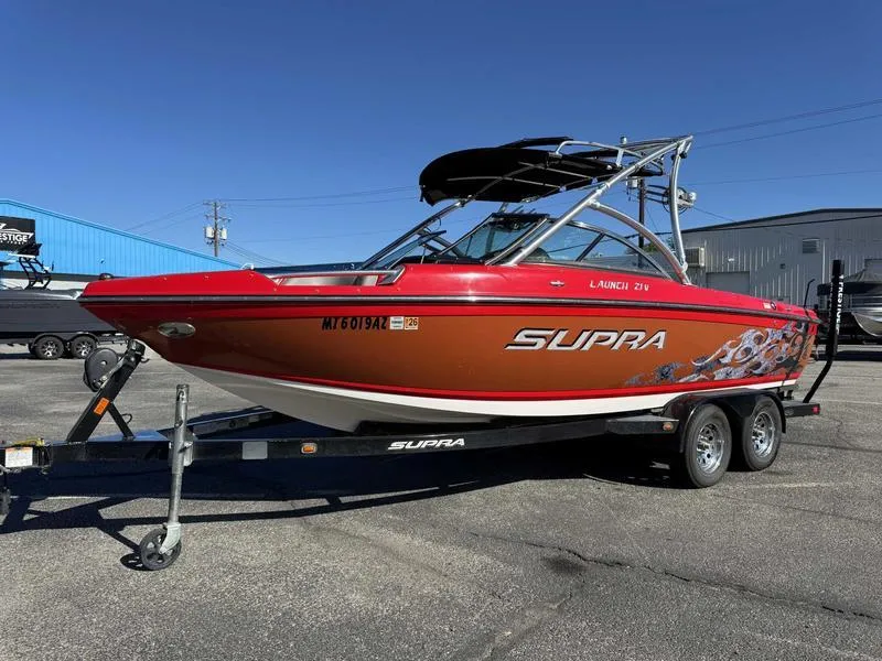 Slide: The Image of 2009 Supra 21V LAUNCH boat on trailer, red and orange design, parked outdoors. - 10
