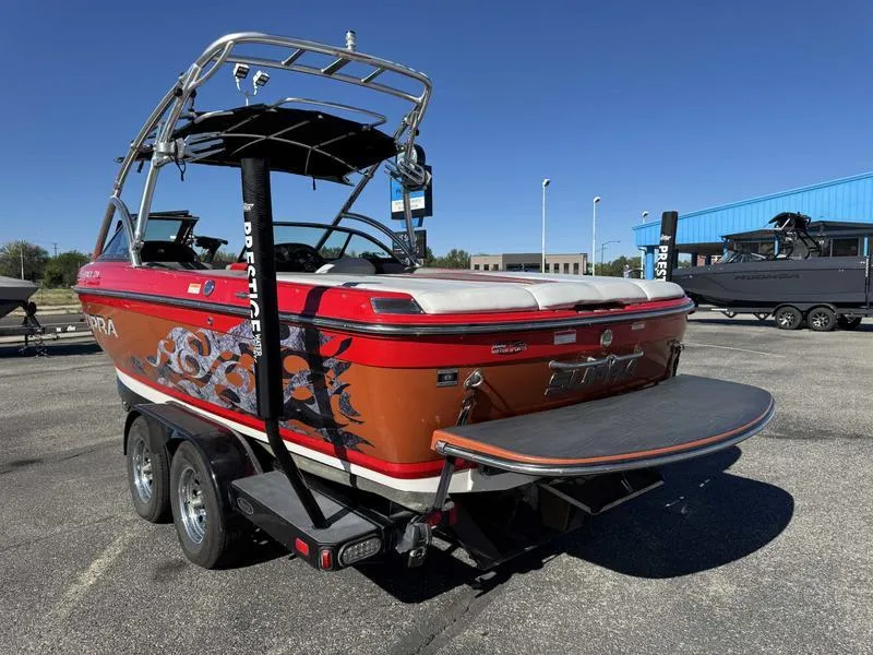 Slide: The Image of 2009 Supra 21V LAUNCH boat on trailer, vibrant orange with graphics, parked outdoors. - 8