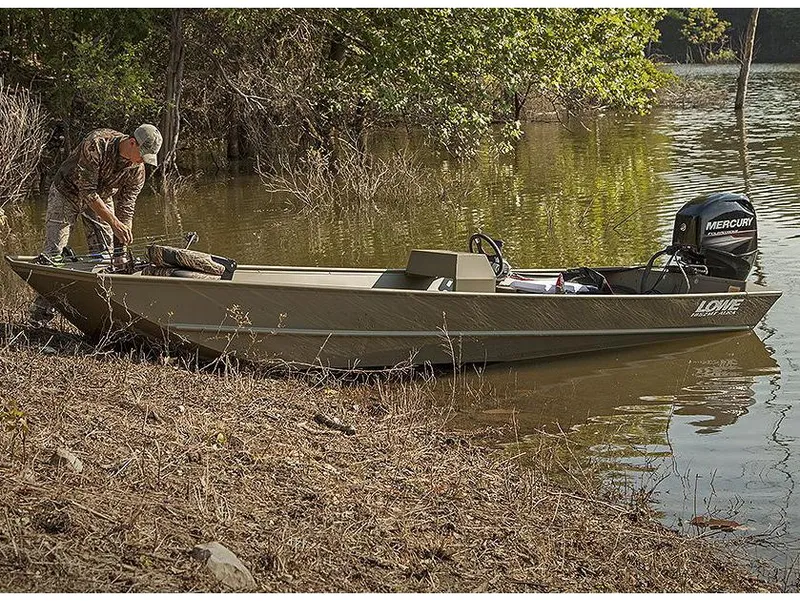 Slide: The Image of Manufacturer Provided Image: 2025 Lowe Jon L1852MT boat by a lake with a person preparing gear. - 10