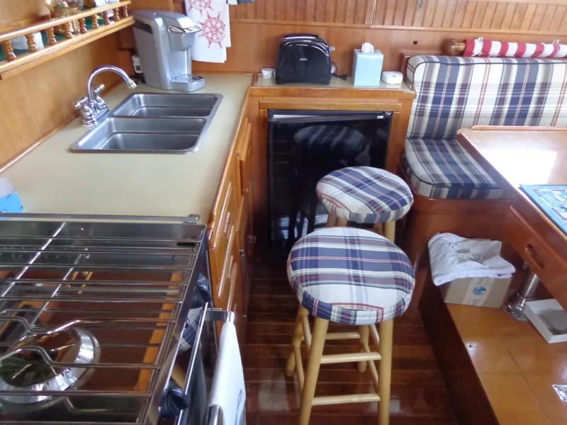 Slide: The Image of 1984 Sundowner Tug Pilothouse kitchen with stove, sink, and plaid stools. - 15