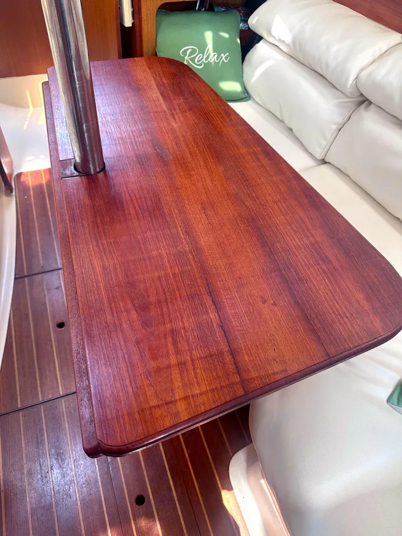 Slide: The Image of Wooden table inside a 1997 Hunter 310 sailboat, with white seating and a "Relax" pillow. - 10