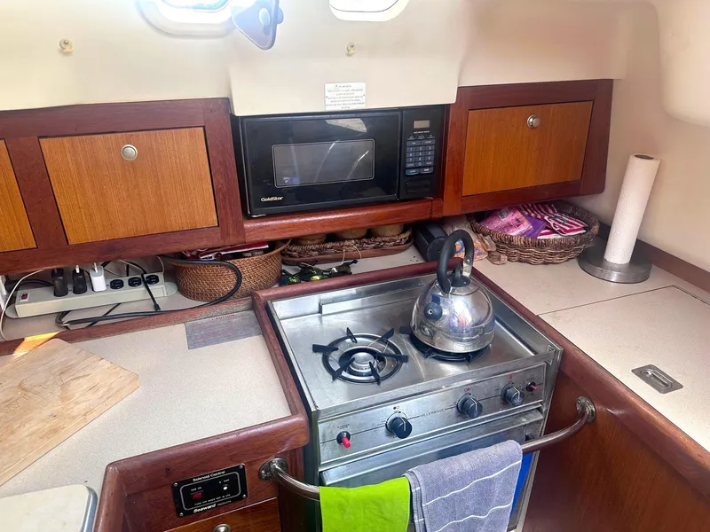 Slide: The Image of Compact kitchen in a 1997 Hunter 310 sailboat with stove, microwave, and wooden cabinets. - 17