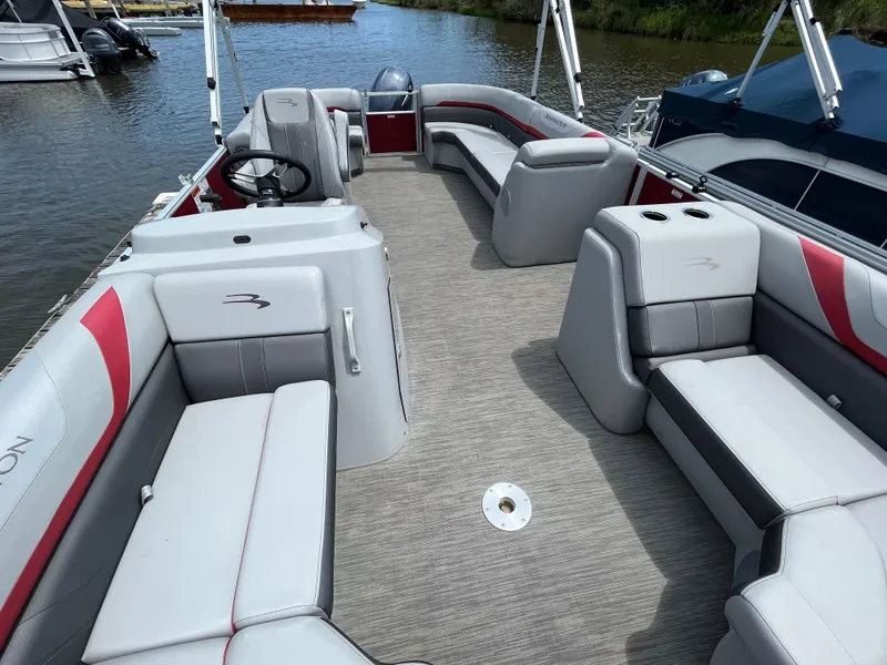 Slide: The Image of 2022 Bennington 22SSRCX pontoon boat interior with gray and red seating, docked on calm water. - 14