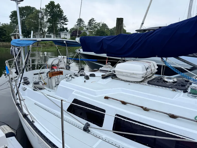 Slide: The Image of 1981 C&C 37 sailboat docked, featuring a blue sail cover and white deck, surrounded by trees. - 5