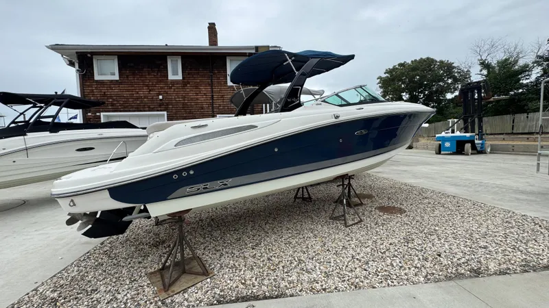 Slide: The Image of 2013 Sea Ray 270 SLX boat on stands, blue and white, near a house. - 2