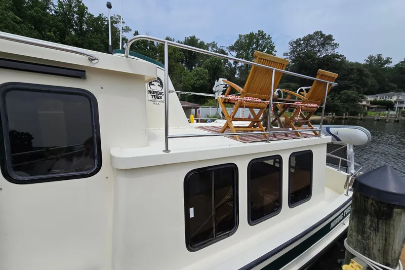Slide: The Image of 2001 Nordic Tug 32 with deck chairs, docked by a scenic waterfront. - 41