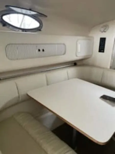 Slide: The Image of 1999 Sea Ray 270 cabin interior with white seating and table, featuring a porthole window. - 9