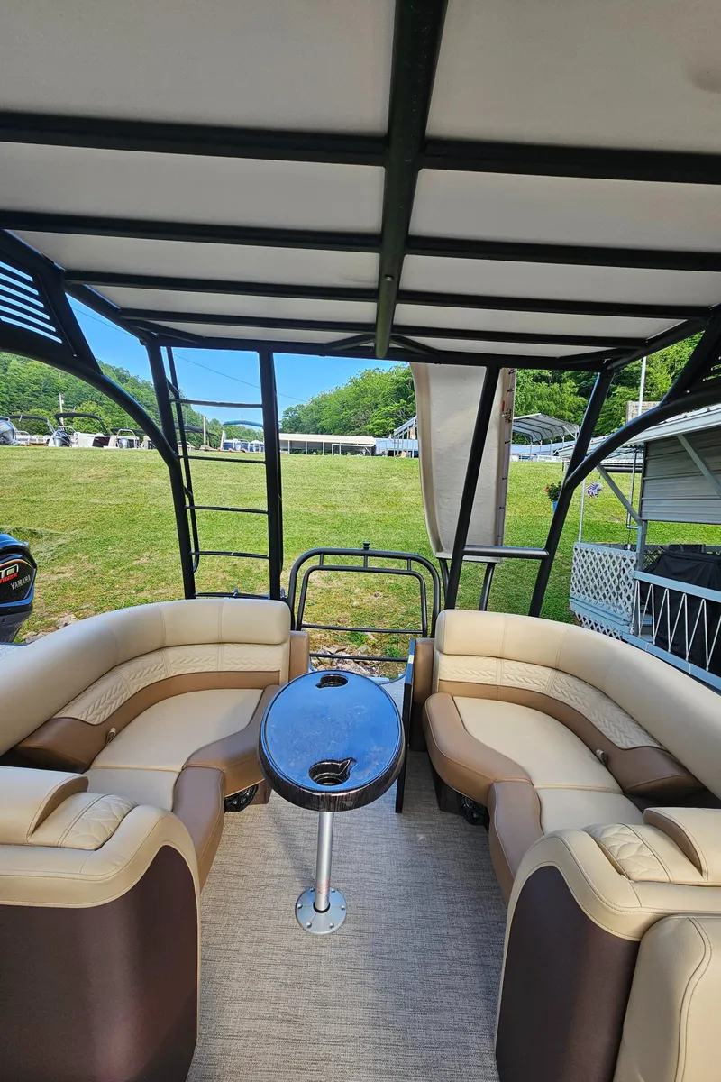 Slide: The Image of 2025 Godfrey MC255 SD boat interior with beige seating and table, parked on grassy area. - 12