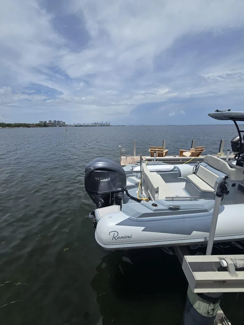 Slide: The Image of 2025 Ranieri CAYMAN 26 SPORT TOURING boat docked by a scenic waterfront. - 6