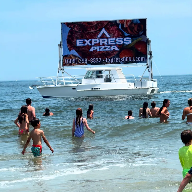 Slide: The Image of Boat with pizza advertisement sails near beachgoers in the ocean. - 1