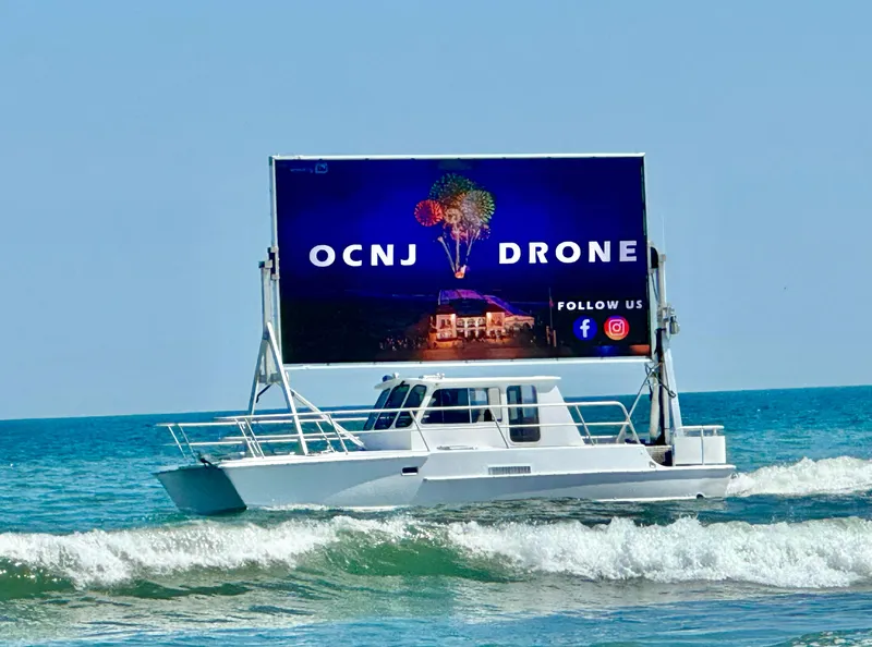 Slide: The Image of Boat with large billboard on ocean, advertising "OCNJ Drone" with social media icons. - 4