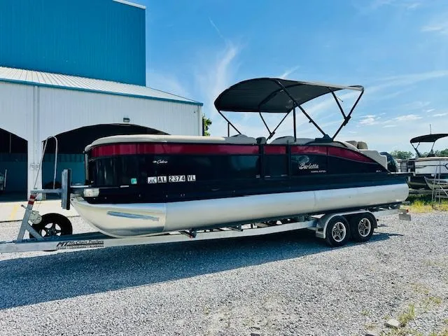 Slide: The Image of 2022 Barletta C24U pontoon boat on trailer, parked near a blue building. - 5
