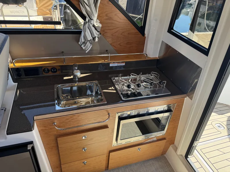 Slide: The Image of 2025 Cutwater C-288 Coupe kitchen with sink, stove, and oven, featuring wood cabinetry and modern design. - 11