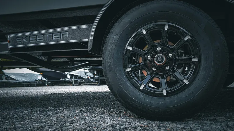 Slide: The Image of 2026 Skeeter ZXE 20 trailer wheel on gravel surface, showcasing sleek black rim design. - 15