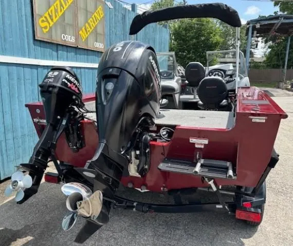 Slide: The Image of 2015 Tracker Targa V-18 Combo boat with dual Mercury outboard motors, parked near a blue building. - 4