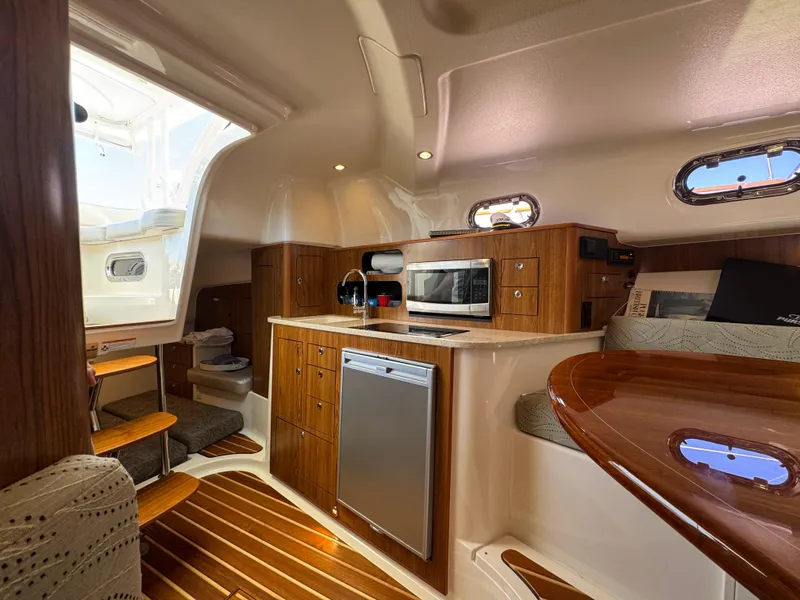 Slide: The Image of 2014 Pursuit 345 OS cabin interior with kitchenette, wooden cabinetry, and seating area. - 14