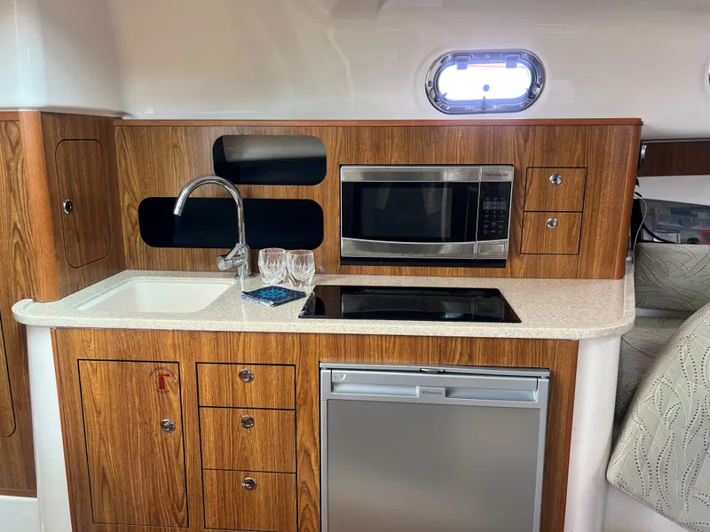 Slide: The Image of 2014 Pursuit 345 OS yacht kitchen with wood cabinetry, sink, microwave, and mini fridge. - 15