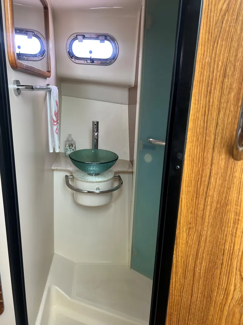 Slide: The Image of 2014 Pursuit 345 OS boat bathroom with glass sink and porthole window. - 17