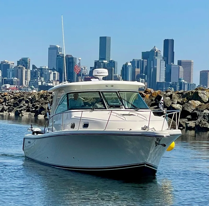 Slide: The Image of 2014 Pursuit 345 OS boat cruising near city skyline and rocky shoreline. - 38
