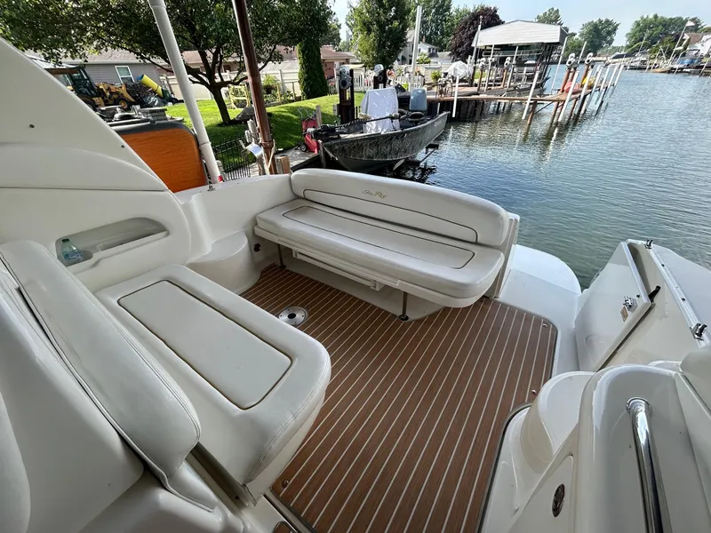 Slide: The Image of 2002 Sea Ray 300 Sundancer boat interior with white seating and wooden deck, docked by a lake. - 9
