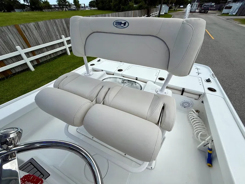 Slide: The Image of 2023 Sea Hunt BX22 boat with cushioned seating and steering wheel, docked near a wooden fence. - 10